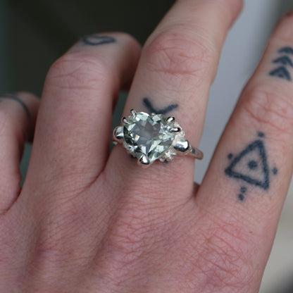 Silver ring with a heart-shaped green mint quartz gemstone decorated with skulls and flowers worn on hand with tattoos
