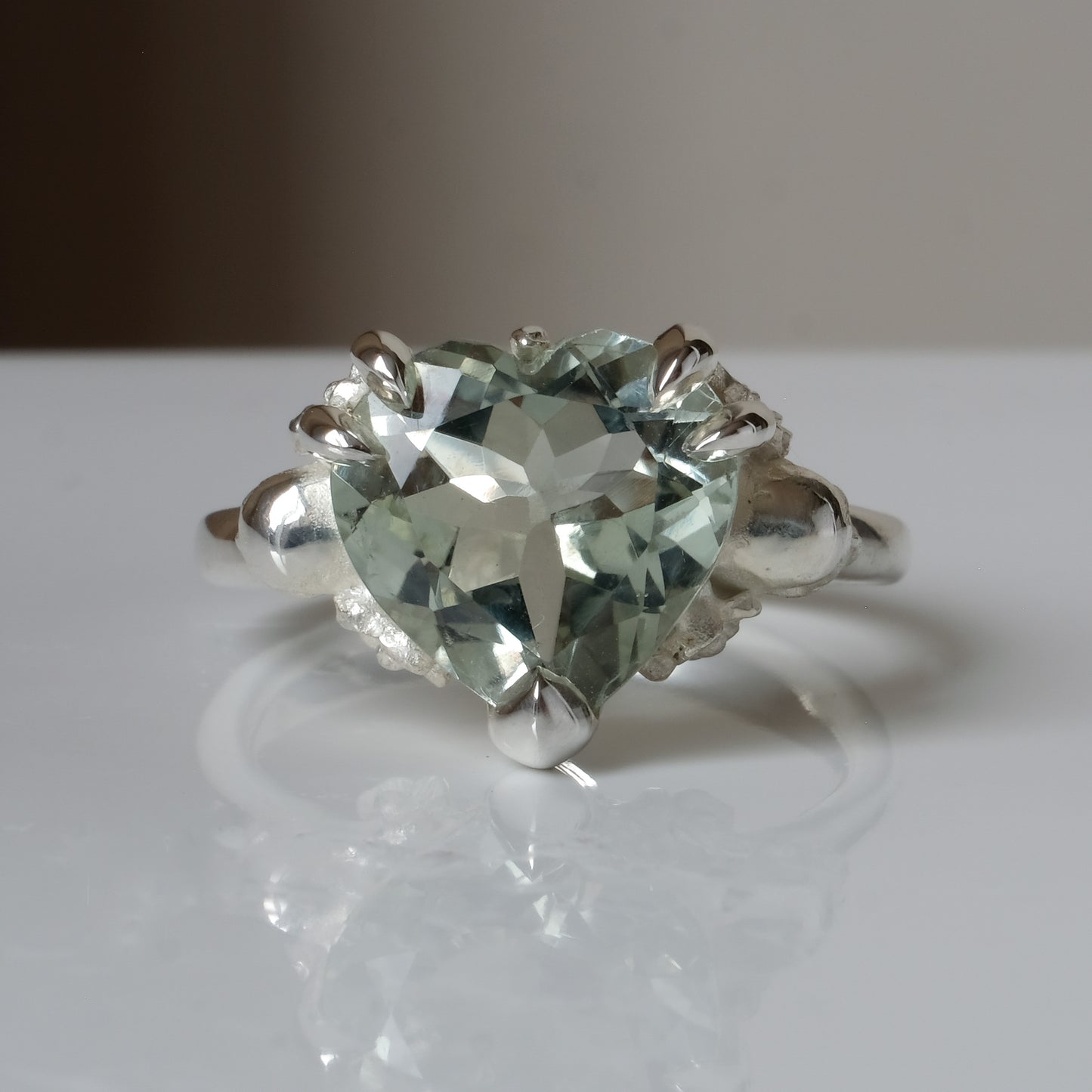 Silver ring with a heart-shaped green mint quartz gemstone decorated with skulls and flowers on a white surface