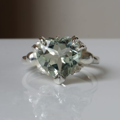 Silver ring with a heart-shaped green mint quartz gemstone decorated with skulls and flowers on a white surface