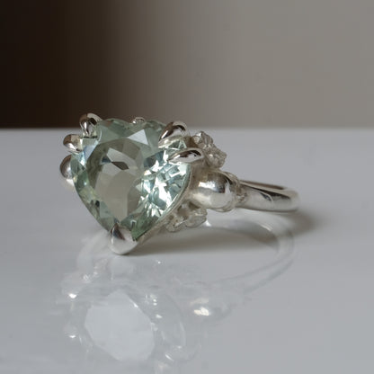 Silver ring with a heart-shaped green mint quartz gemstone decorated with skulls and flowers on a white surface