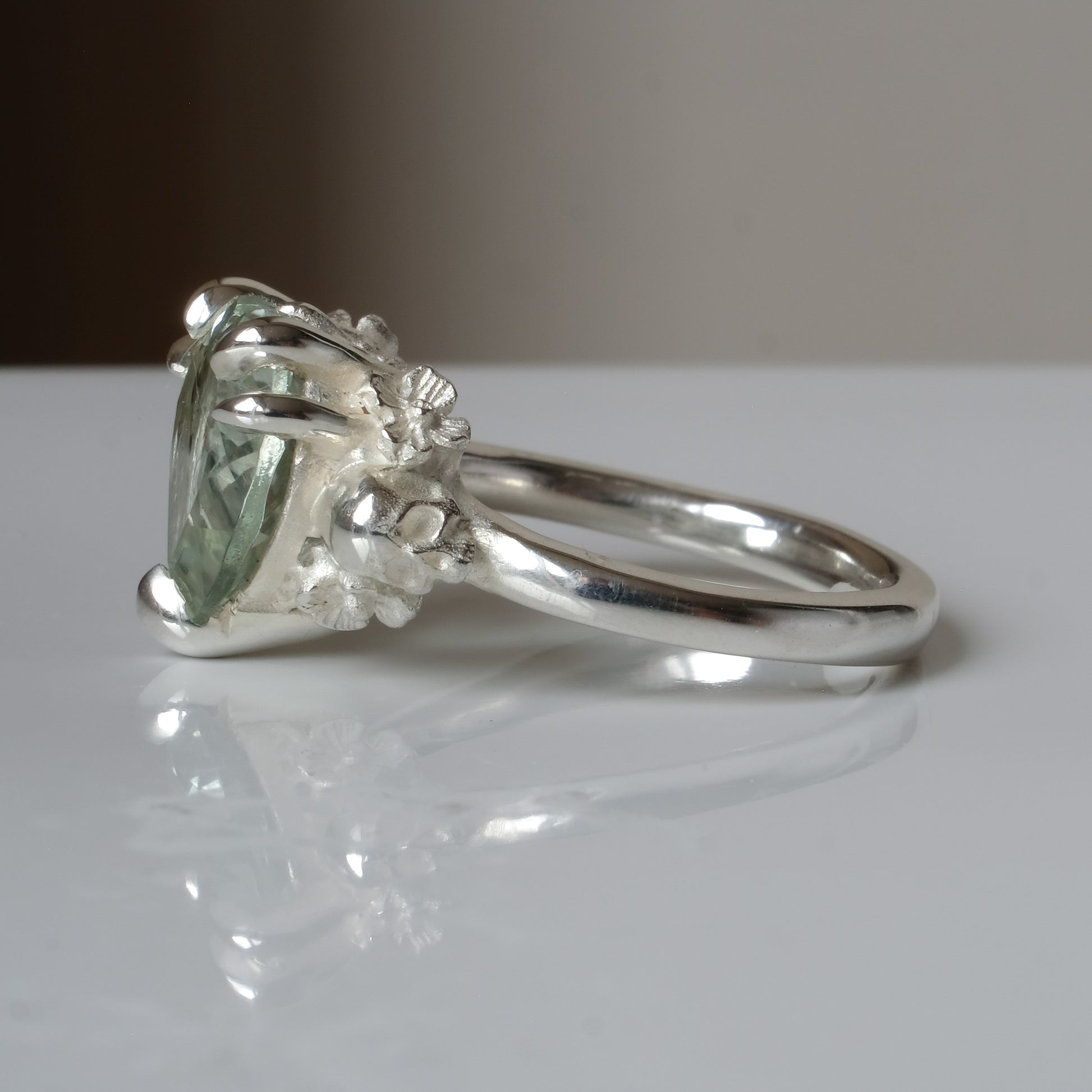 Silver ring with a heart-shaped green mint quartz gemstone decorated with skulls and flowers on a white surface