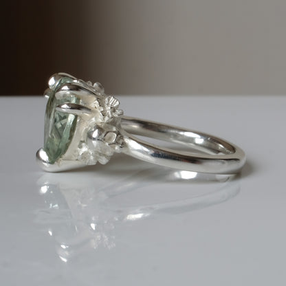 Silver ring with a heart-shaped green mint quartz gemstone decorated with skulls and flowers on a white surface