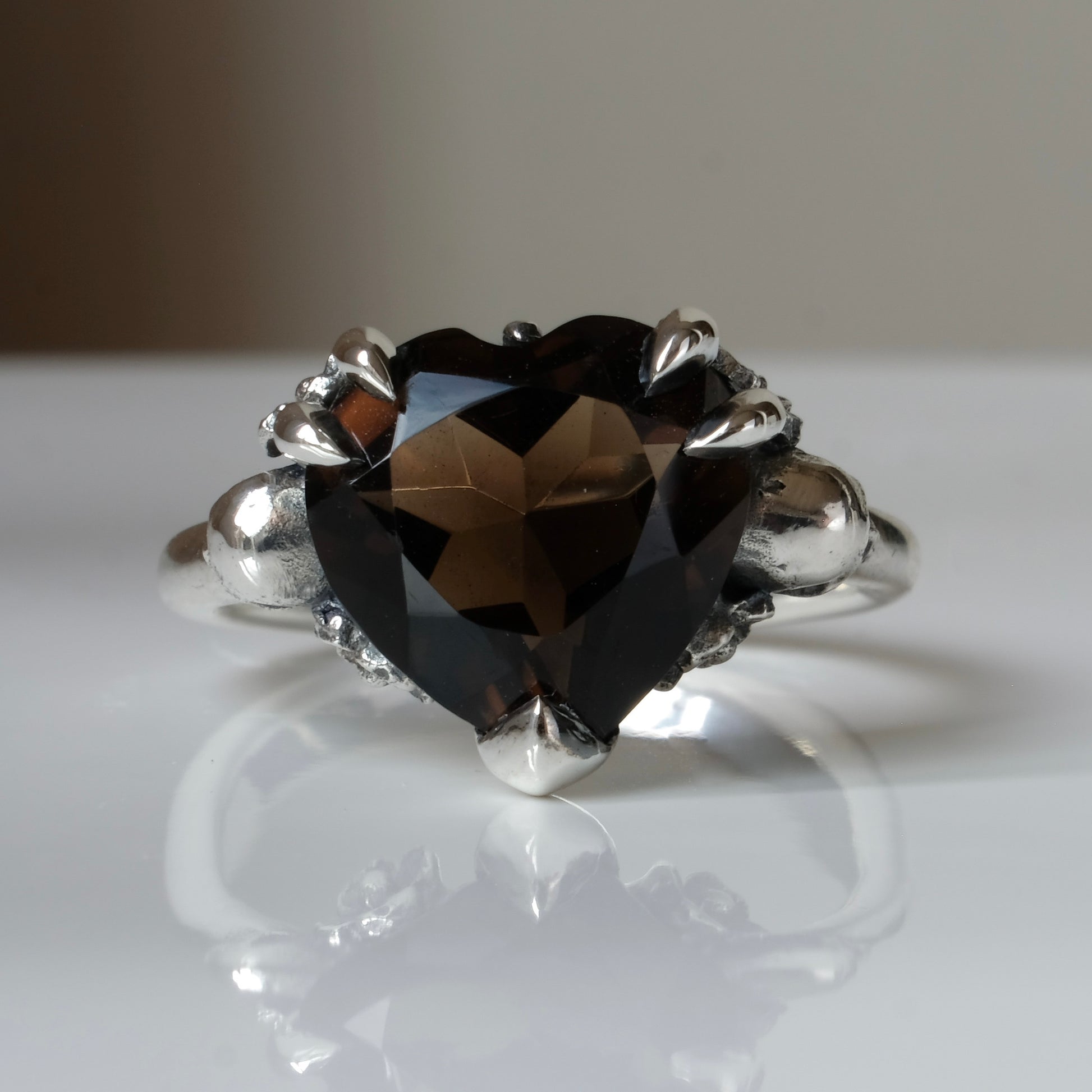 Silver ring with a heart-shaped brown smokey quartz gemstone decorated with skulls and flowers on a white surface