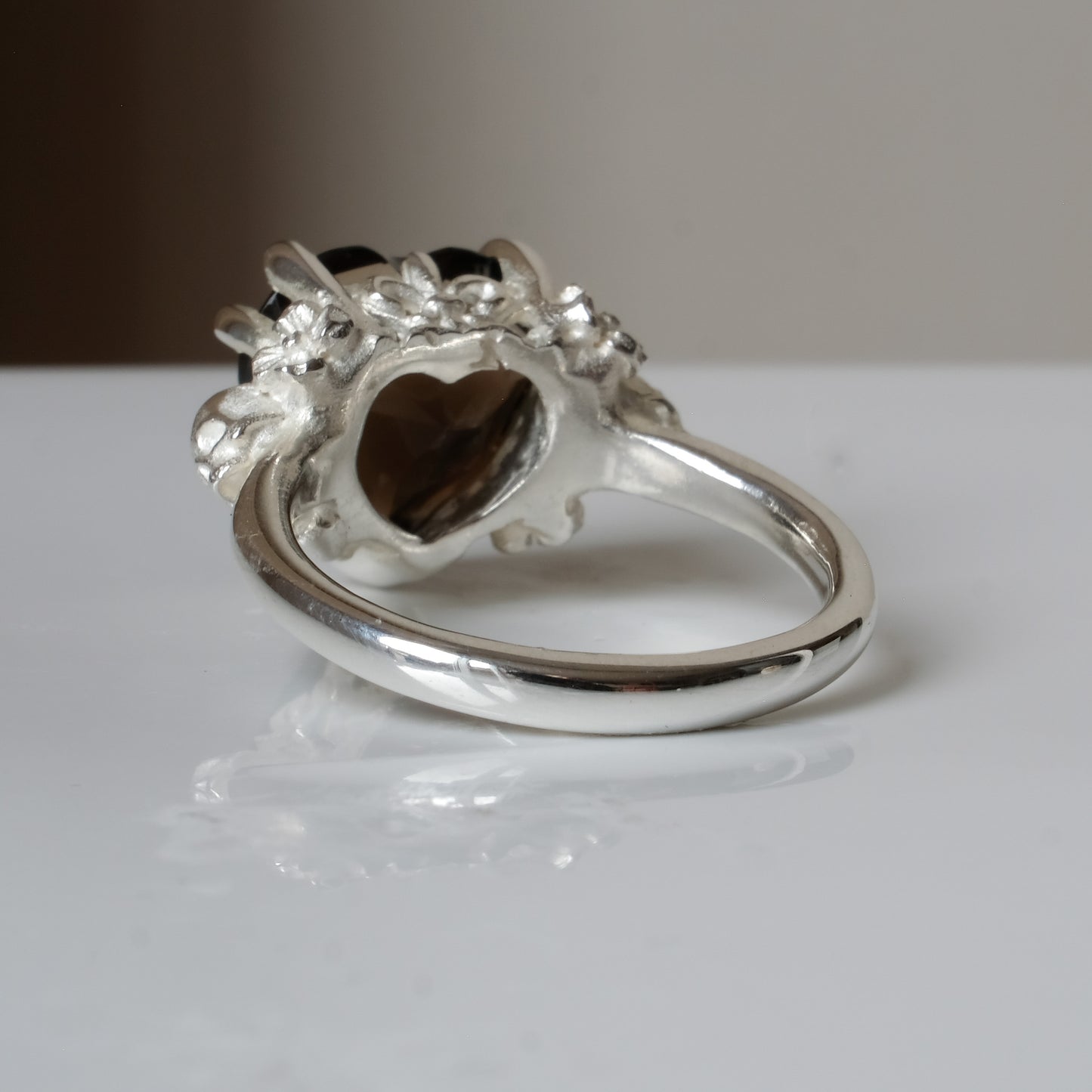 Silver ring with a heart-shaped brown smokey quartz gemstone decorated with skulls and flowers on a white surface
