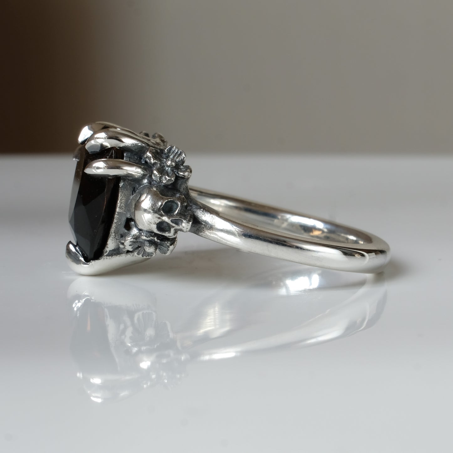 Silver ring with a heart-shaped brown smokey quartz gemstone decorated with skulls and flowers on a white surface