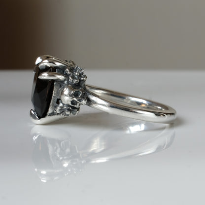 Silver ring with a heart-shaped brown smokey quartz gemstone decorated with skulls and flowers on a white surface