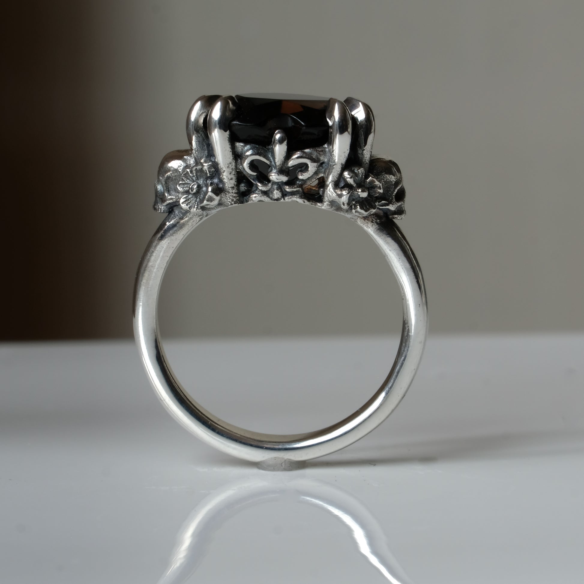 Silver ring with a heart-shaped brown smokey quartz gemstone decorated with skulls and flowers on a white surface