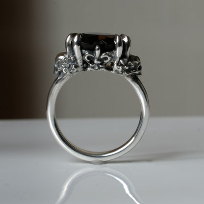 Silver ring with a heart-shaped brown smokey quartz gemstone decorated with skulls and flowers on a white surface
