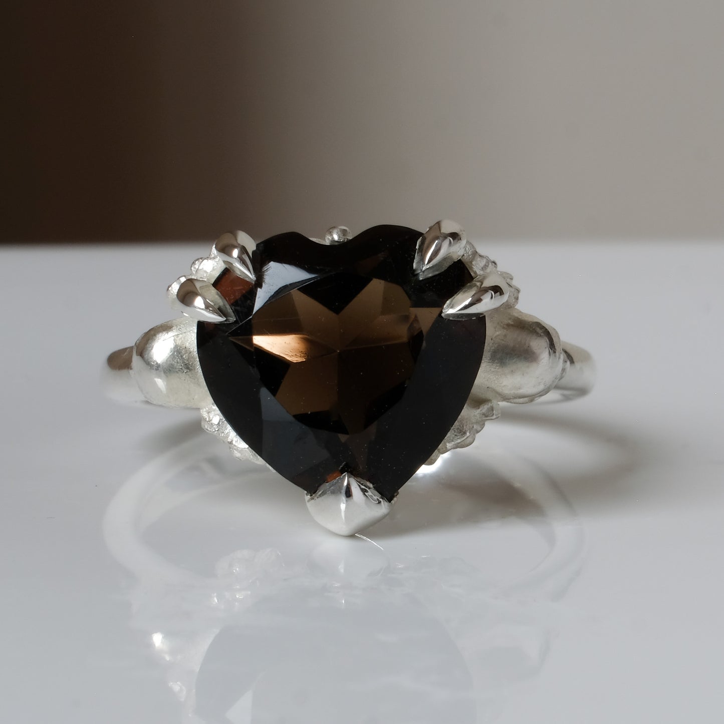 Silver ring with a heart-shaped brown smokey quartz gemstone decorated with skulls and flowers on a white surface