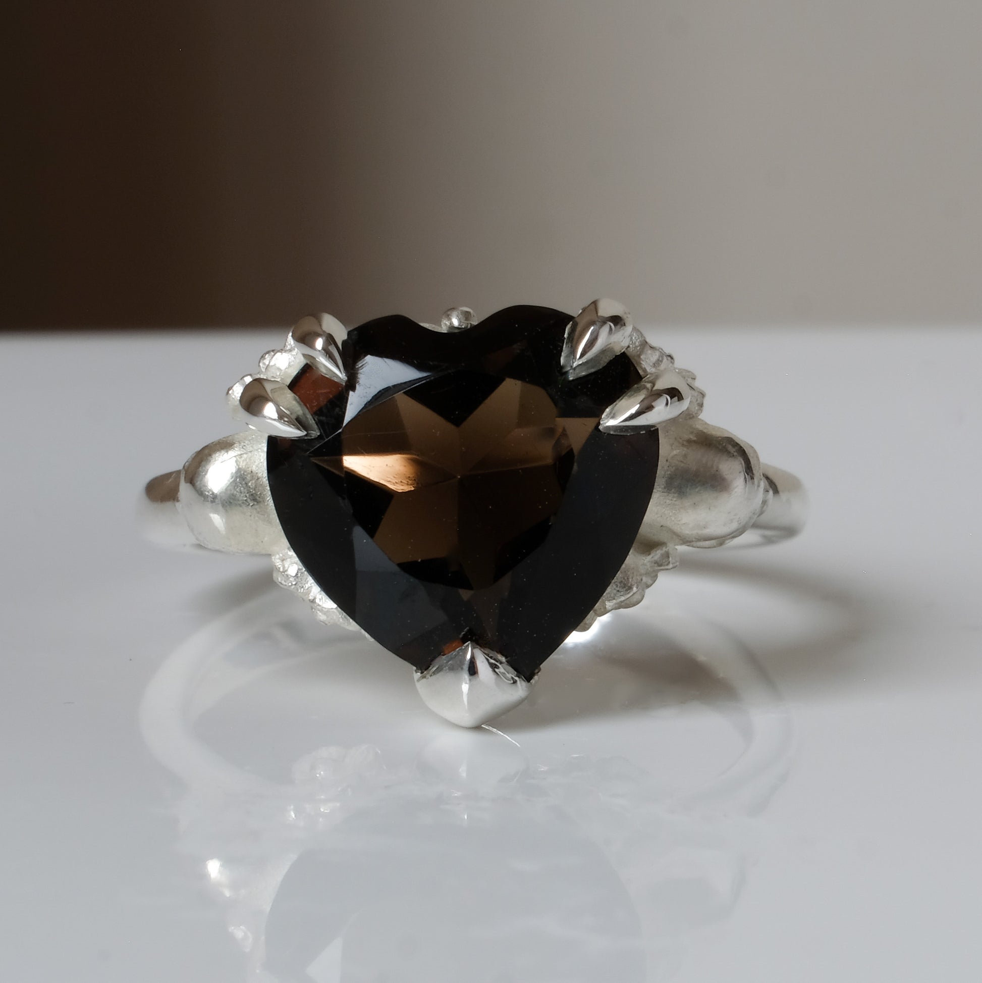 Silver ring with a heart-shaped brown smokey quartz gemstone decorated with skulls and flowers on a white surface
