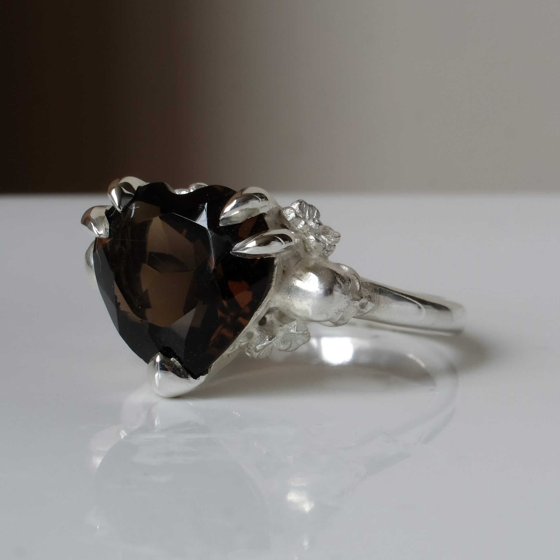 Silver ring with a heart-shaped brown smokey quartz gemstone decorated with skulls and flowers on a white surface