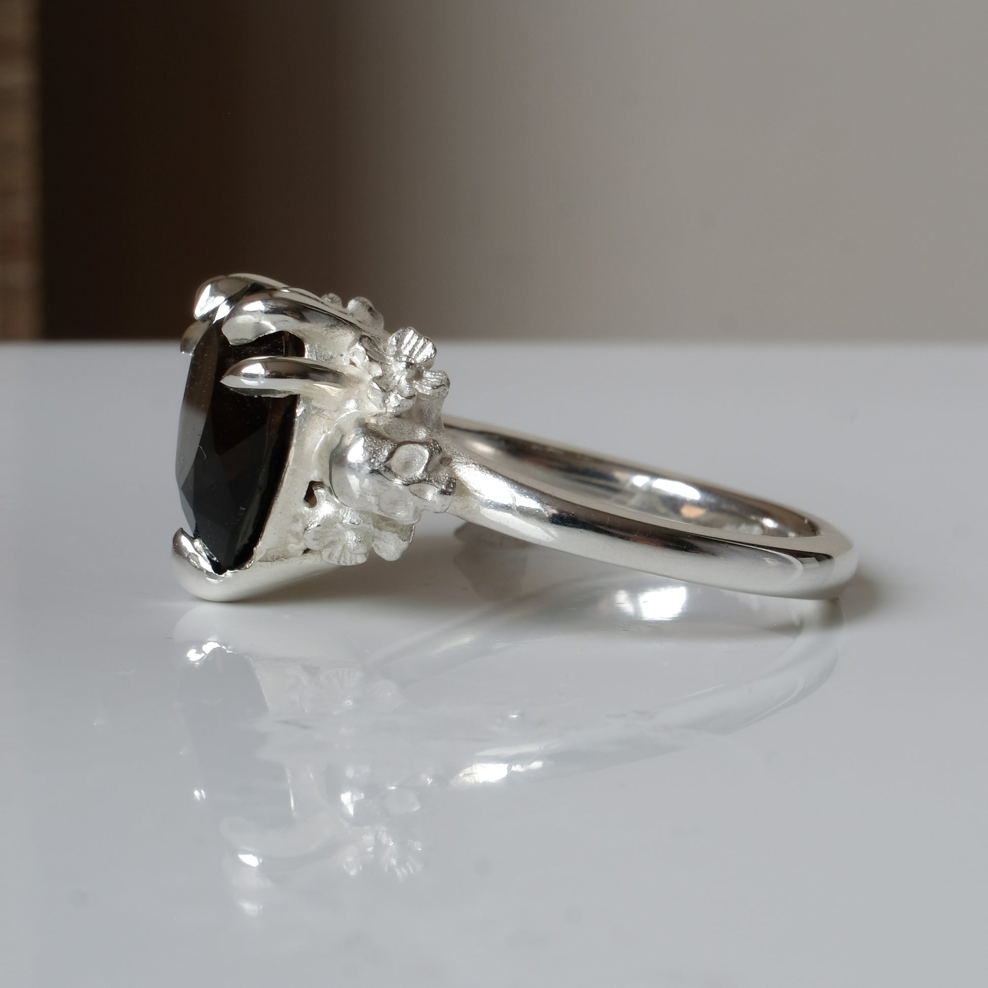 Silver ring with a heart-shaped brown smokey quartz gemstone decorated with skulls and flowers on a white surface
