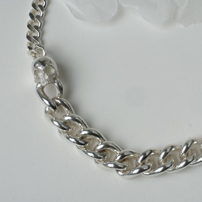 Heavy weight sterling silver curb link chain descending in size. 9ct yellow gold skulls hang off center from links. Handmade in London by Charlie Shires