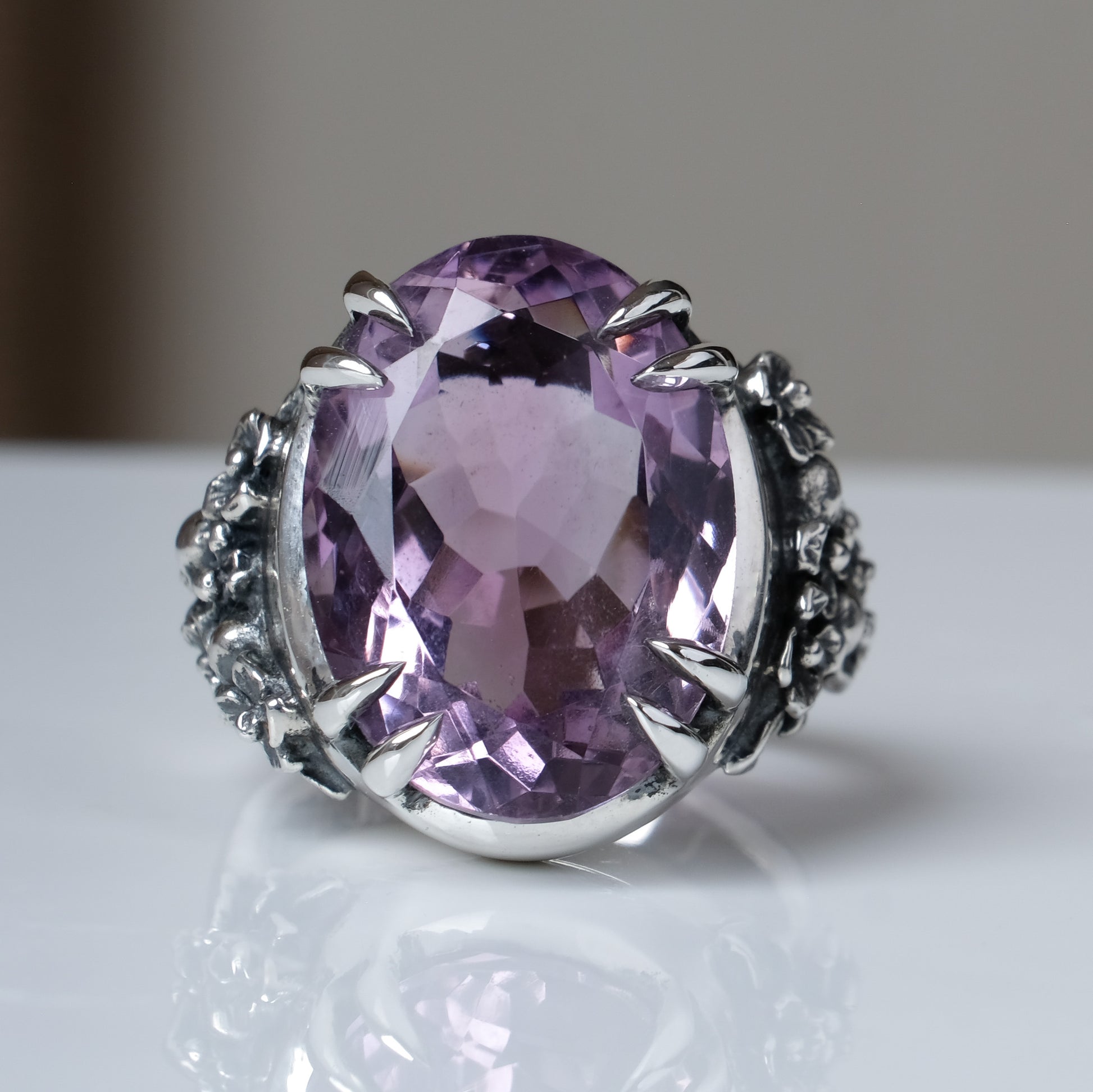 Ring claw set with large amethyst gemstone with skull and floral detail on side.  made in sterling silver on white background