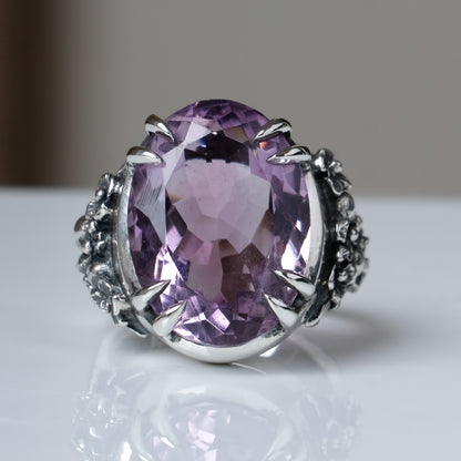 Ring claw set with large amethyst gemstone with skull and floral detail on side.  made in sterling silver on white background