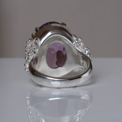 Ring claw set with large amethyst gemstone with skull and floral detail on side.  made in sterling silver on reflective surface