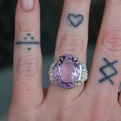 Ring claw set with large amethyst gemstone with skull and floral detail on side.  made in sterling silver worn on hand with tattoos