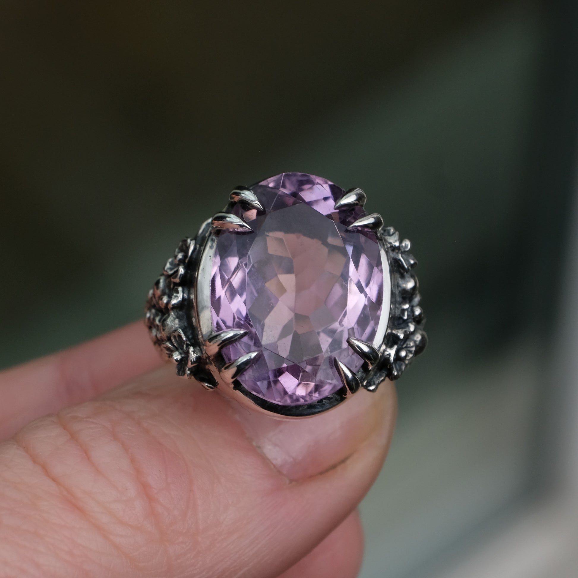 Ring claw set with large amethyst gemstone with skull and floral detail on side.  made in sterling silver on reflective surface