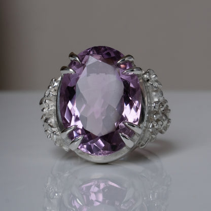 Ring claw set with large amethyst gemstone with skull and floral detail on side.  made in sterling silver on reflective surface