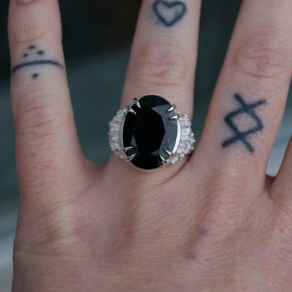 Ring claw set with large black spinel gemstone with skull and floral detail on side.  made in sterling silver worn on hand with tattoos