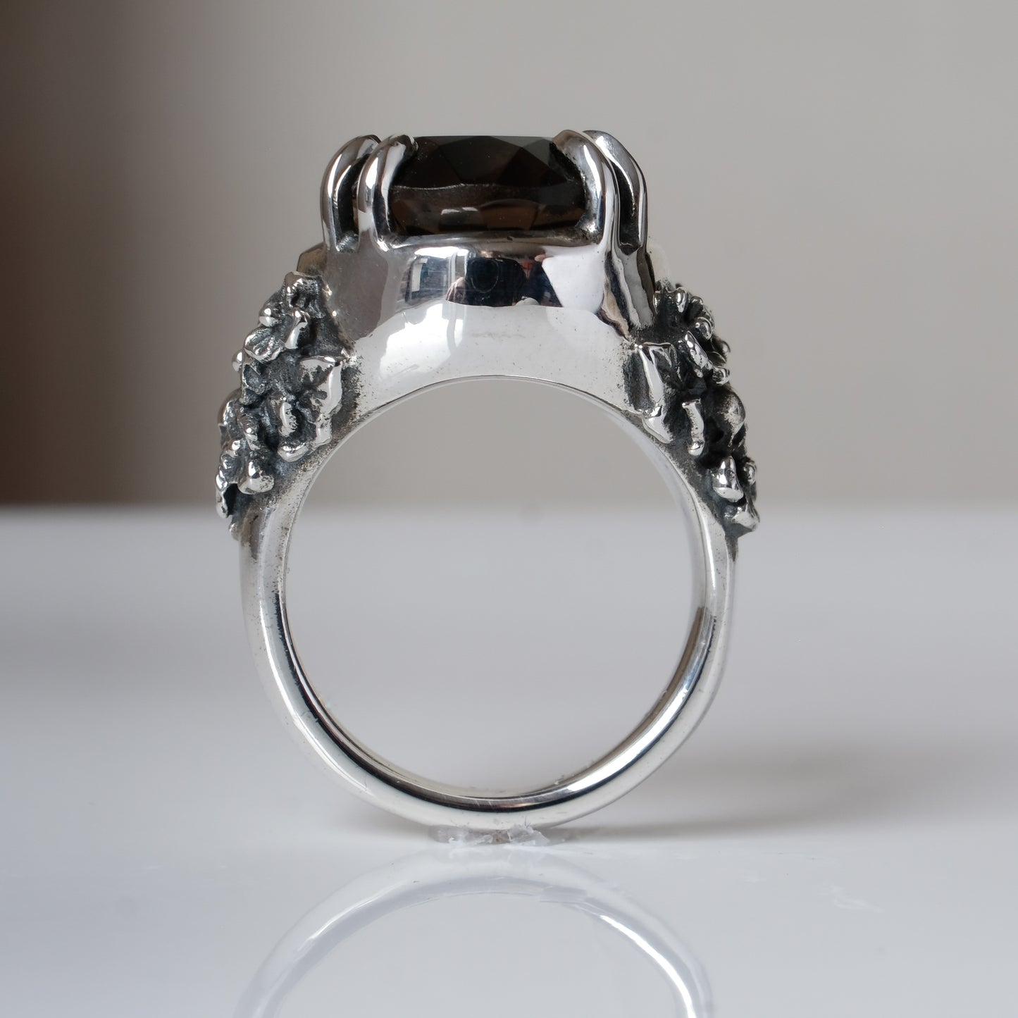 Ring claw set with large black spinel gemstone with skull and floral detail on side.  made in sterling silver on reflective surface