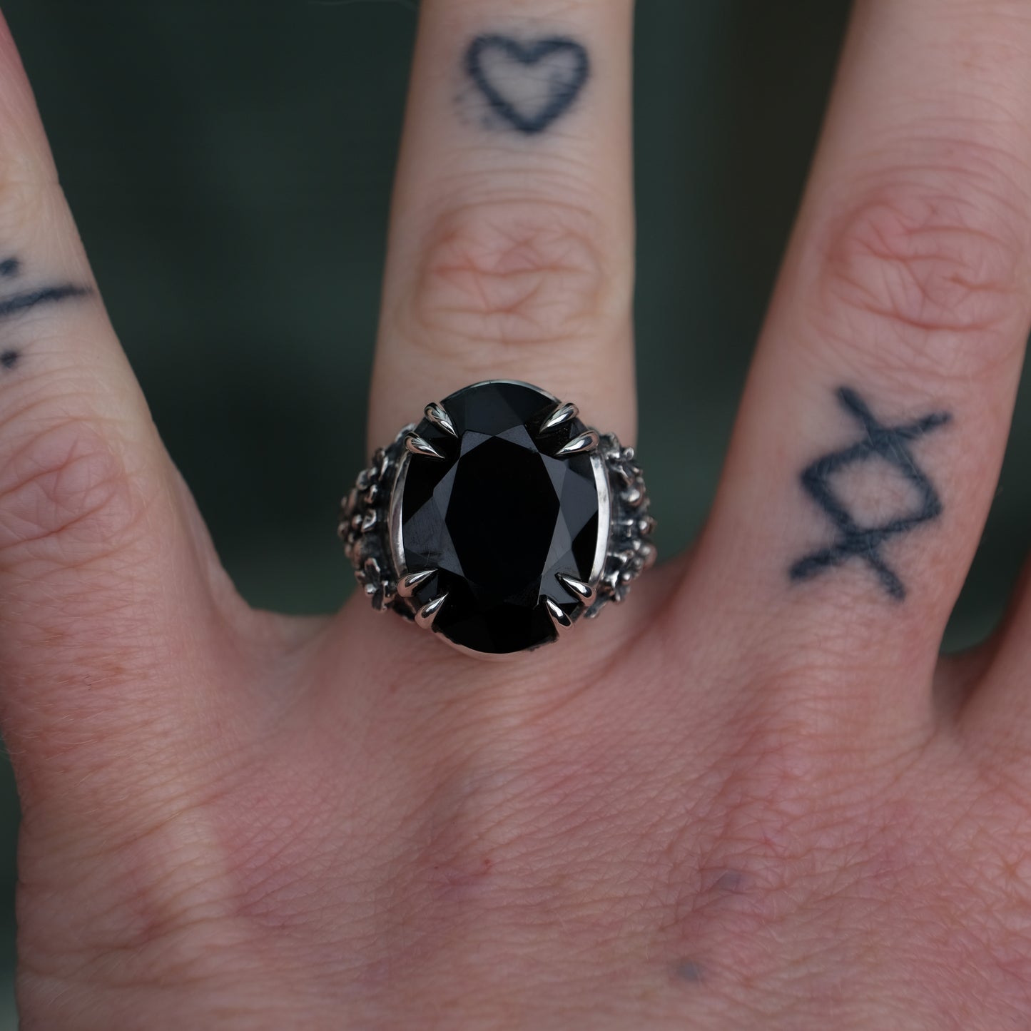Ring claw set with large black spinel gemstone with skull and floral detail on side.  made in sterling silver worn on hand with tattoos