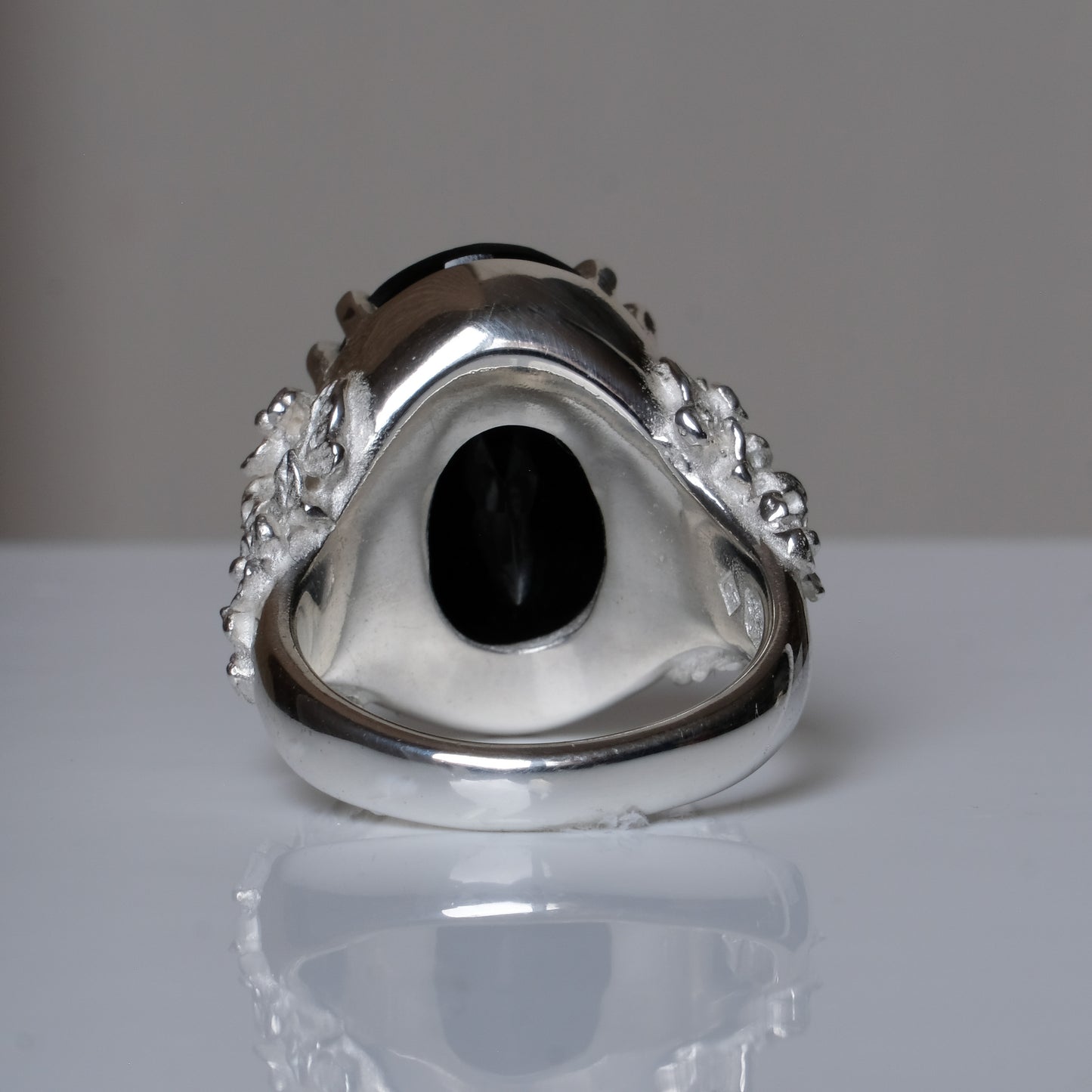 Ring claw set with large black spinel gemstone with skull and floral detail on side.  made in sterling silver on reflective surface