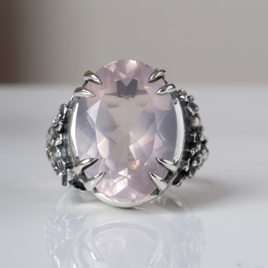 Ring claw set with large rose quartz gemstone with skull and floral detail on side.  made in sterling silver on reflective surface