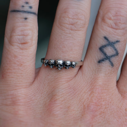 Sterling silver eternity ring with 5 skulls descending in size photographed on hand. Handmade in London by Charlie Shires