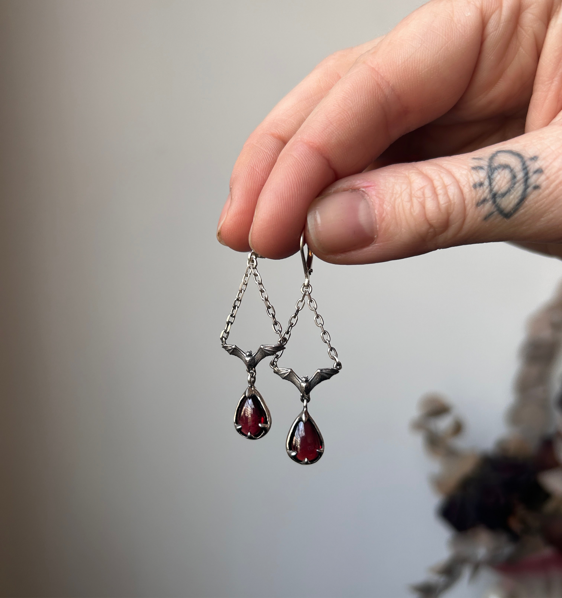 Bat earrings with hanging claw set pear shaped garnet, drop earrings made in sterling silver by Charlie Shires