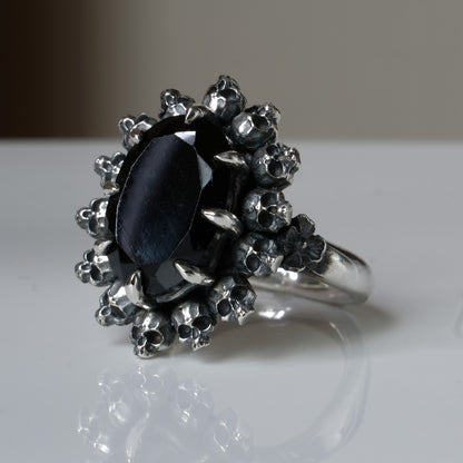 Ring with claw set black spinel gemstone and silver skull design on a white background