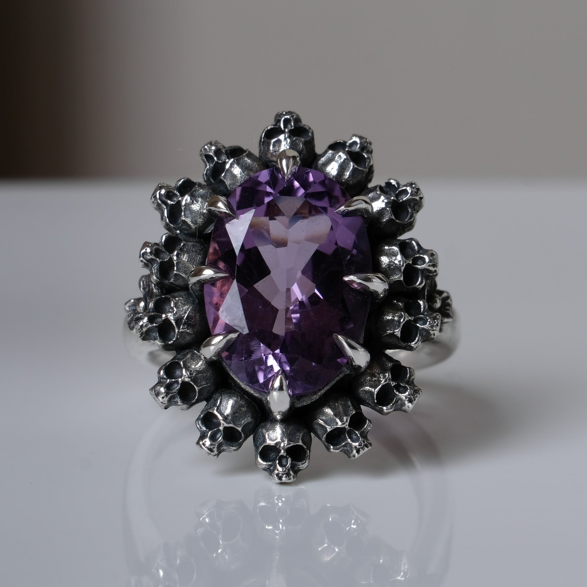 Ring with claw set amethyst and silver skull design on a white background