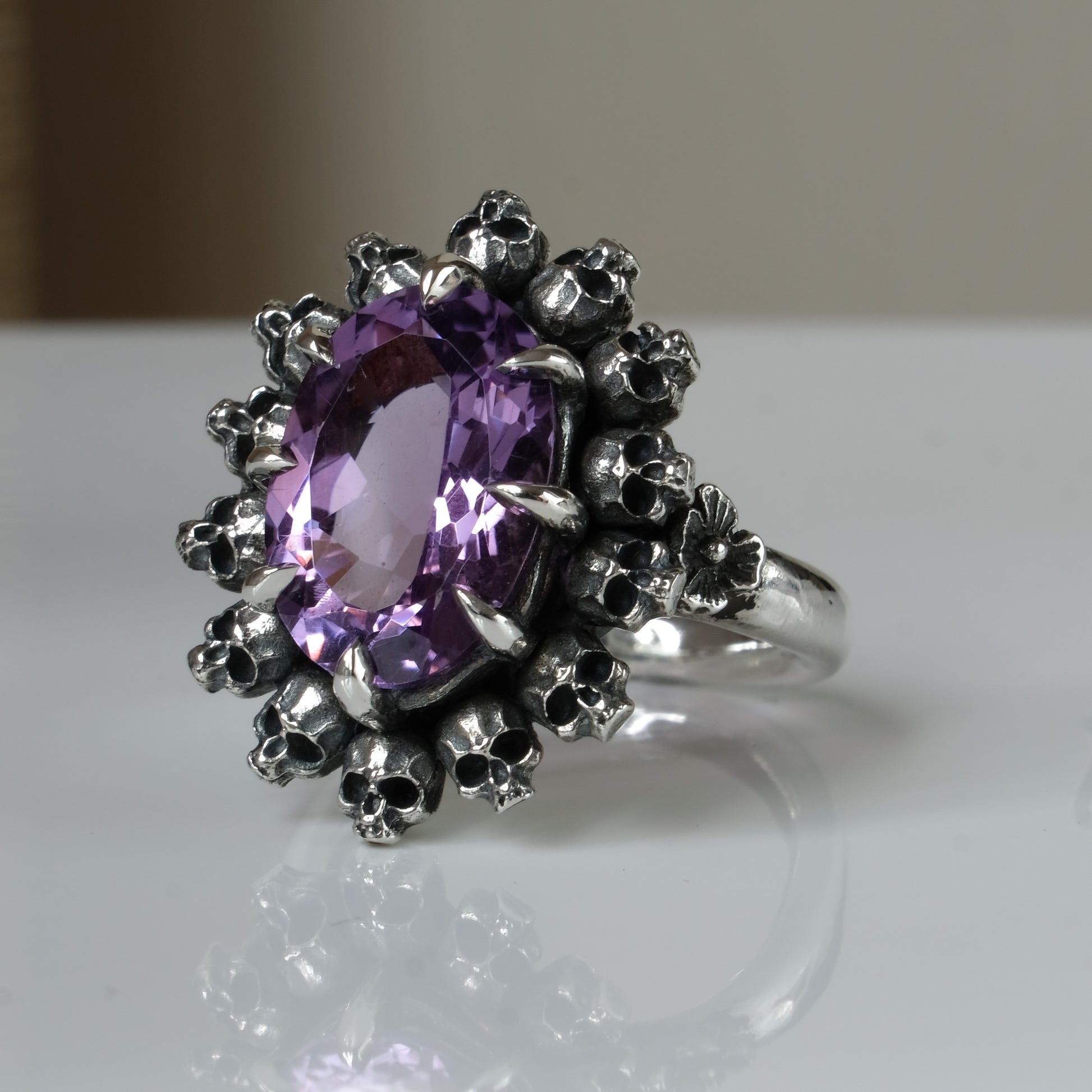 Ring with claw set amethyst gemstone and silver skull design on a white background