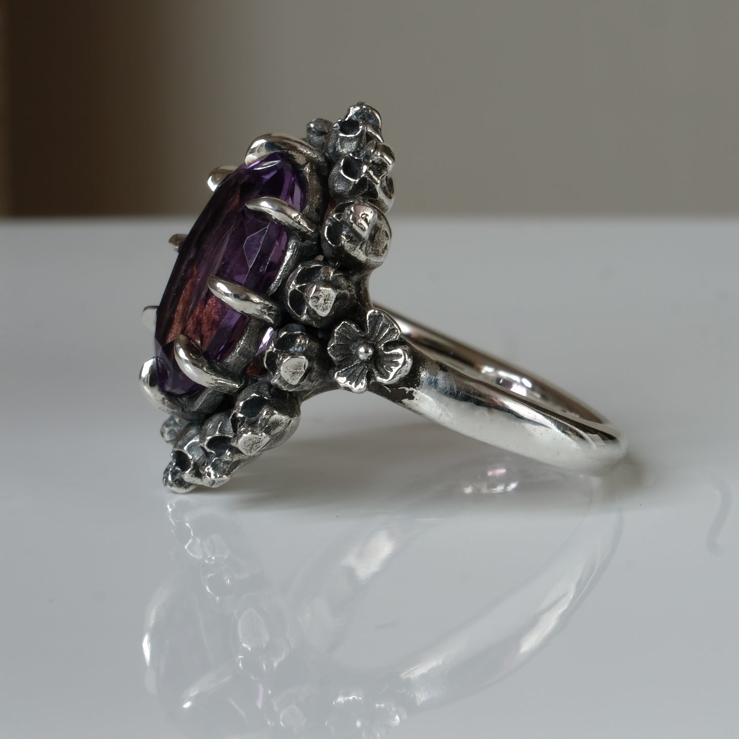 Ring with claw set amethyst gemstone and silver skull design on a white background
