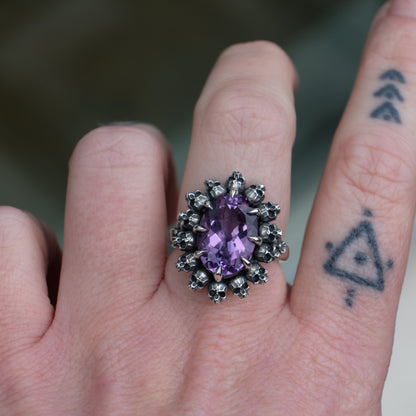 Ring with claw set amethyst gemstone and silver skull design worn on hand with tattoos