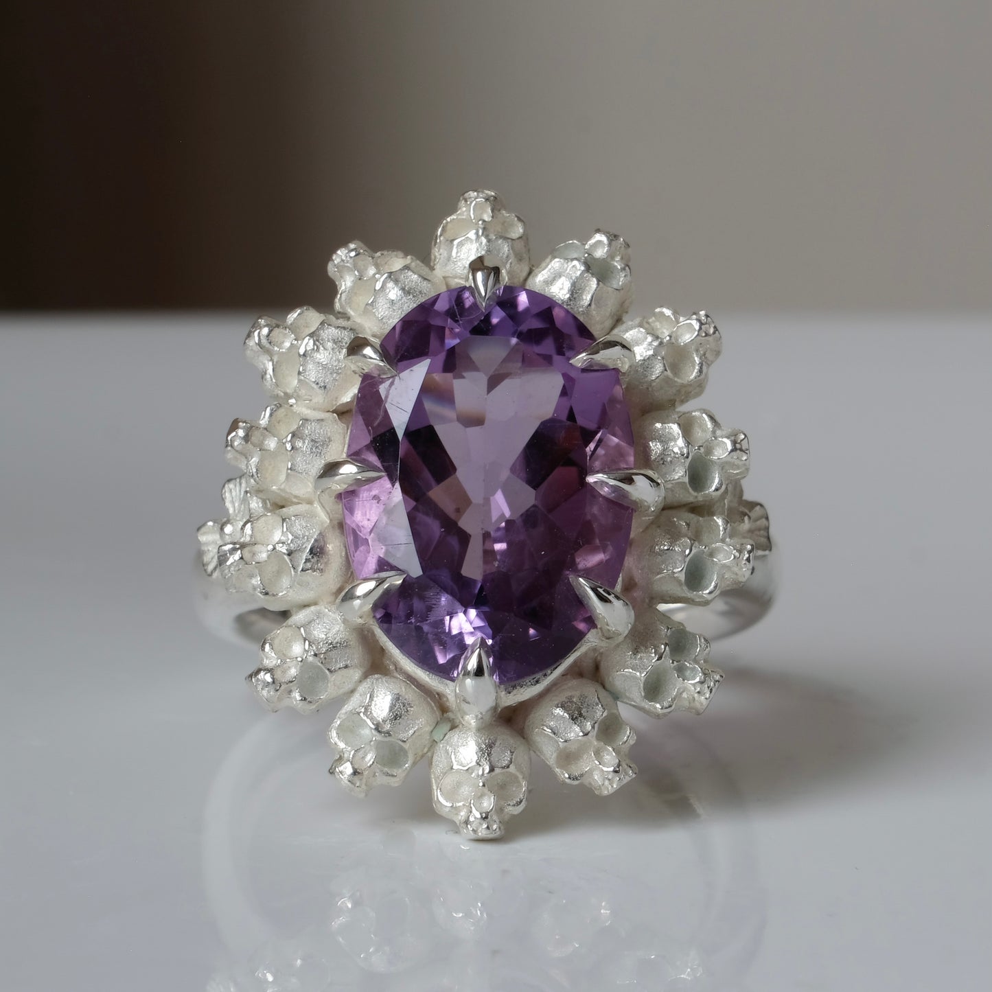 Ring with claw set amethyst gemstone and silver skull design on a white background