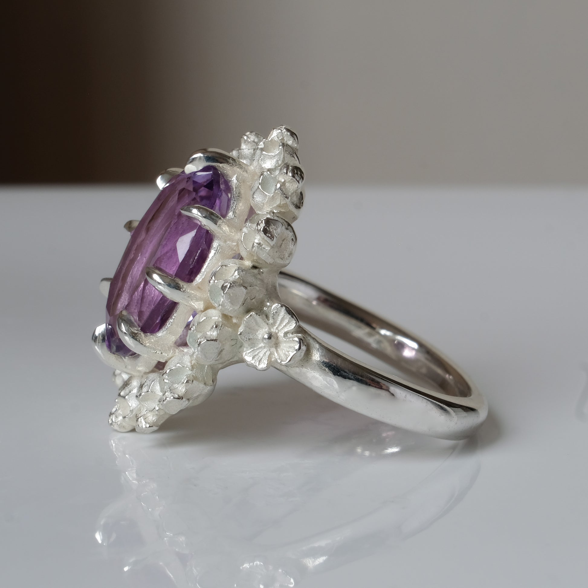 Ring with claw set amethyst gemstone and silver skull design on a white background