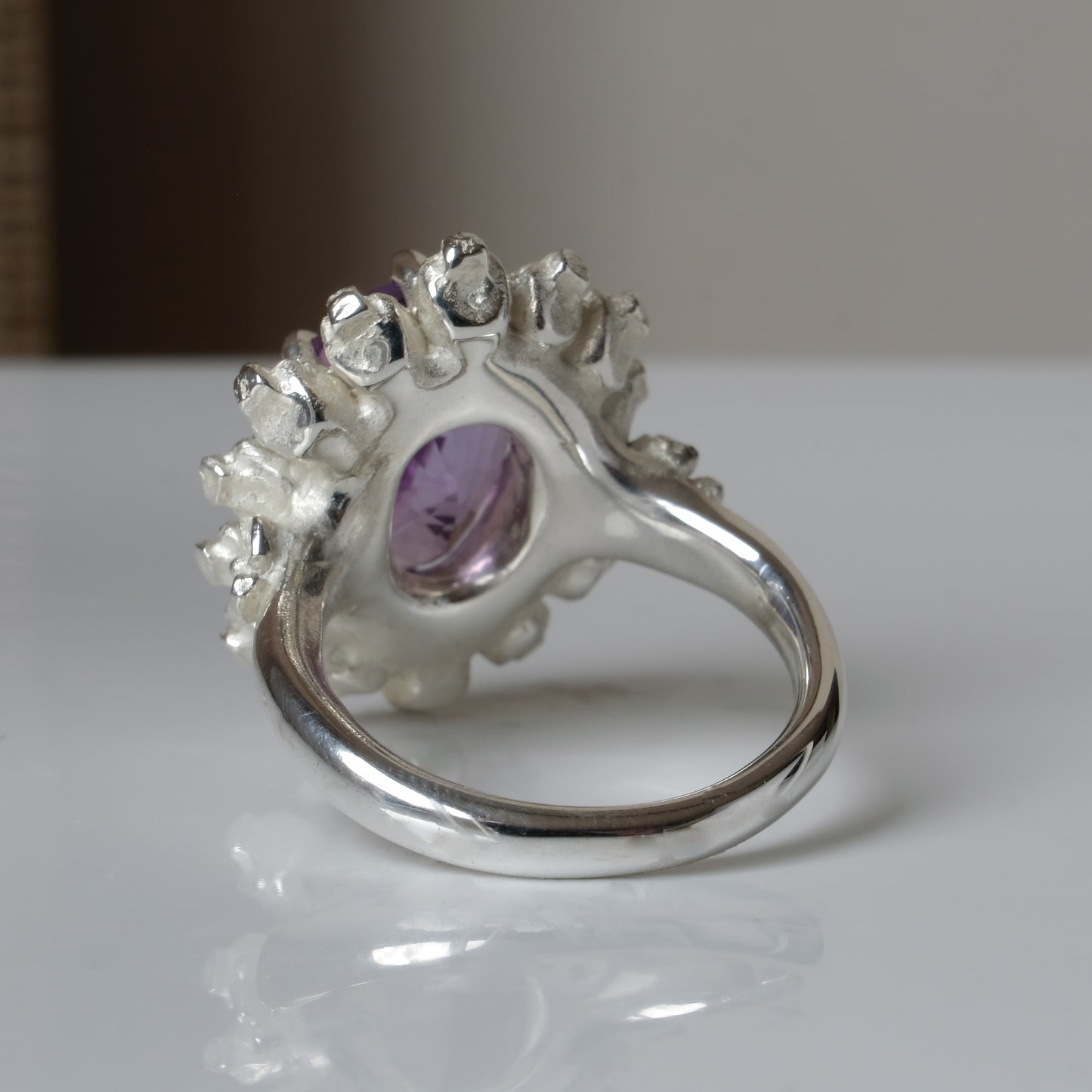 Ring with claw set amethyst gemstone and silver skull design on a white background