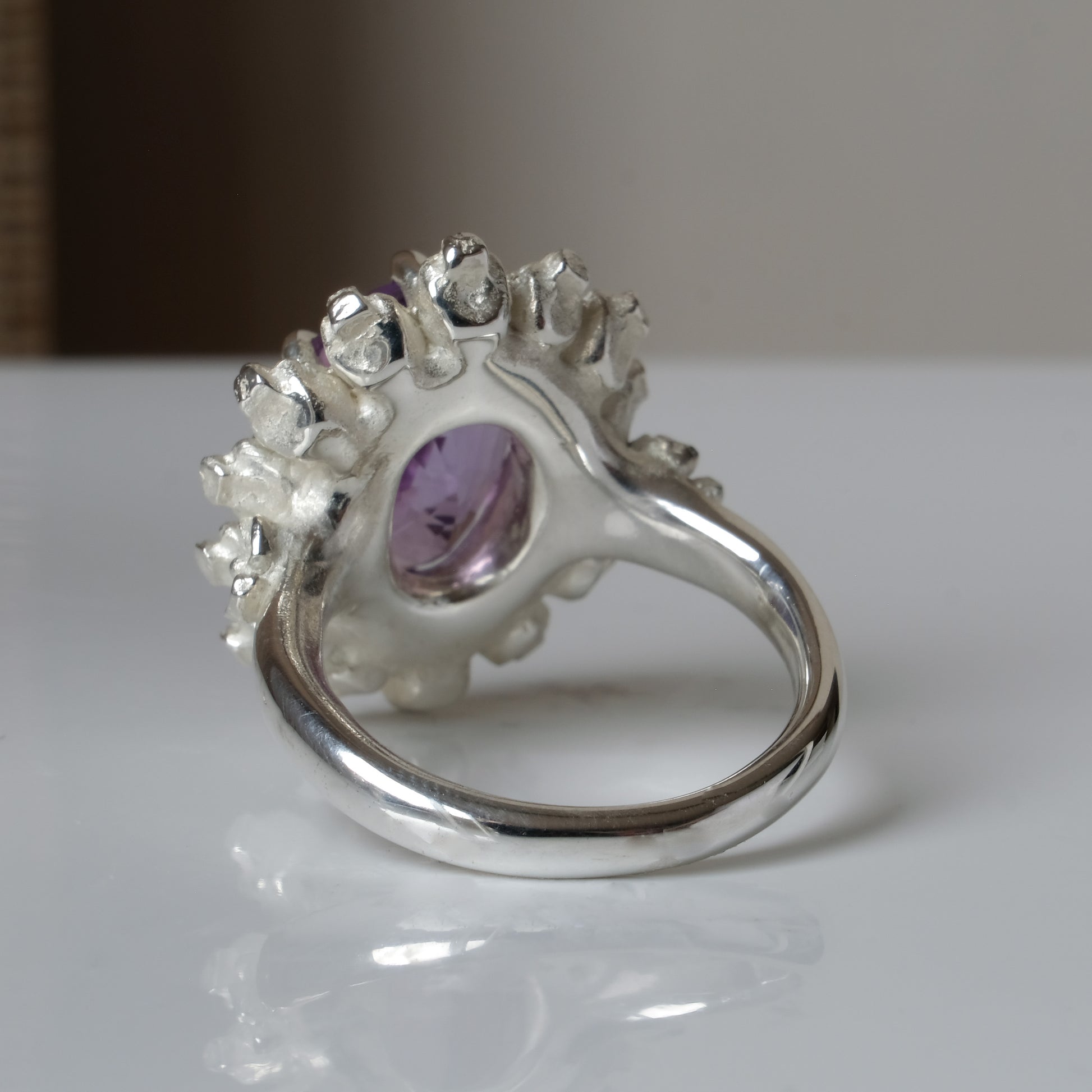 Ring with claw set amethyst gemstone and silver skull design on a white background