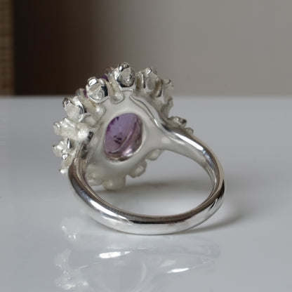 Ring with claw set amethyst gemstone and silver skull design on a white background
