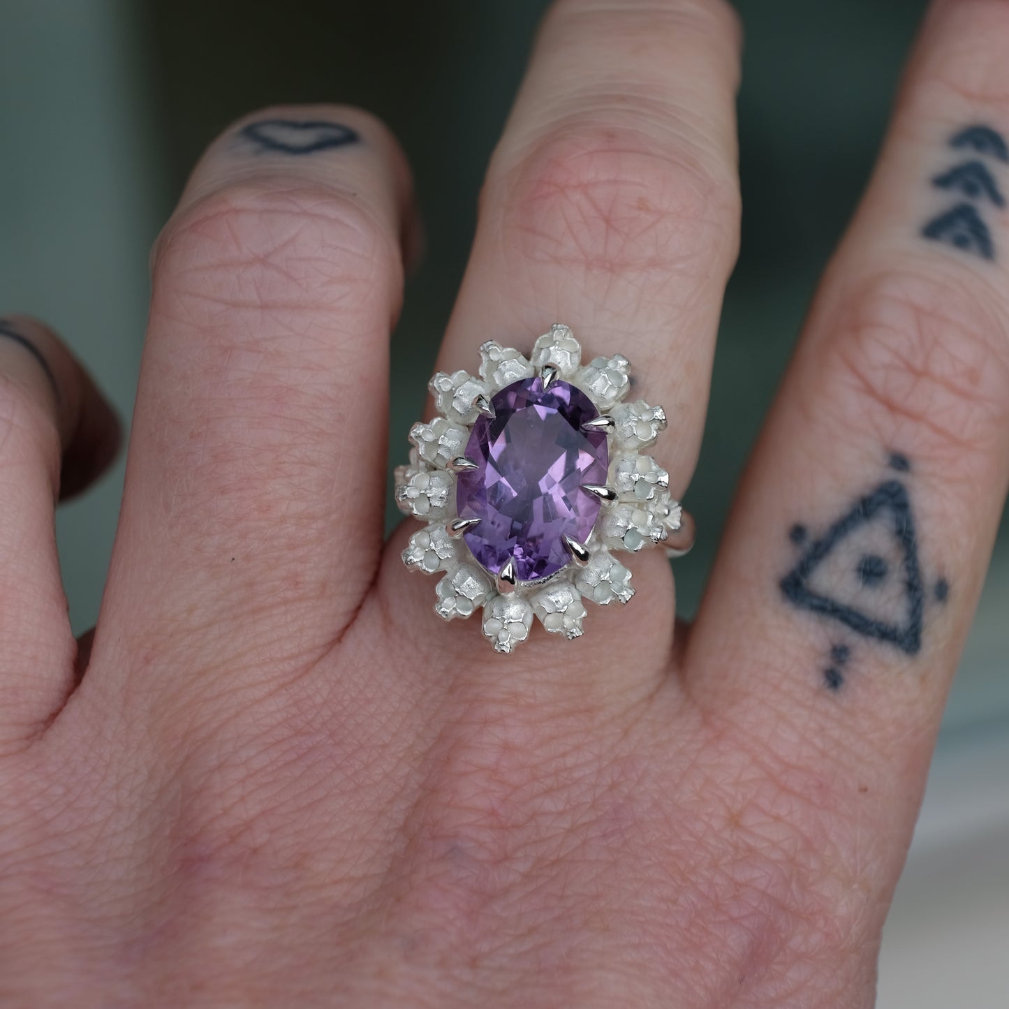 Ring with claw set amethyst gemstone and silver skull design worn on hand with tattoos