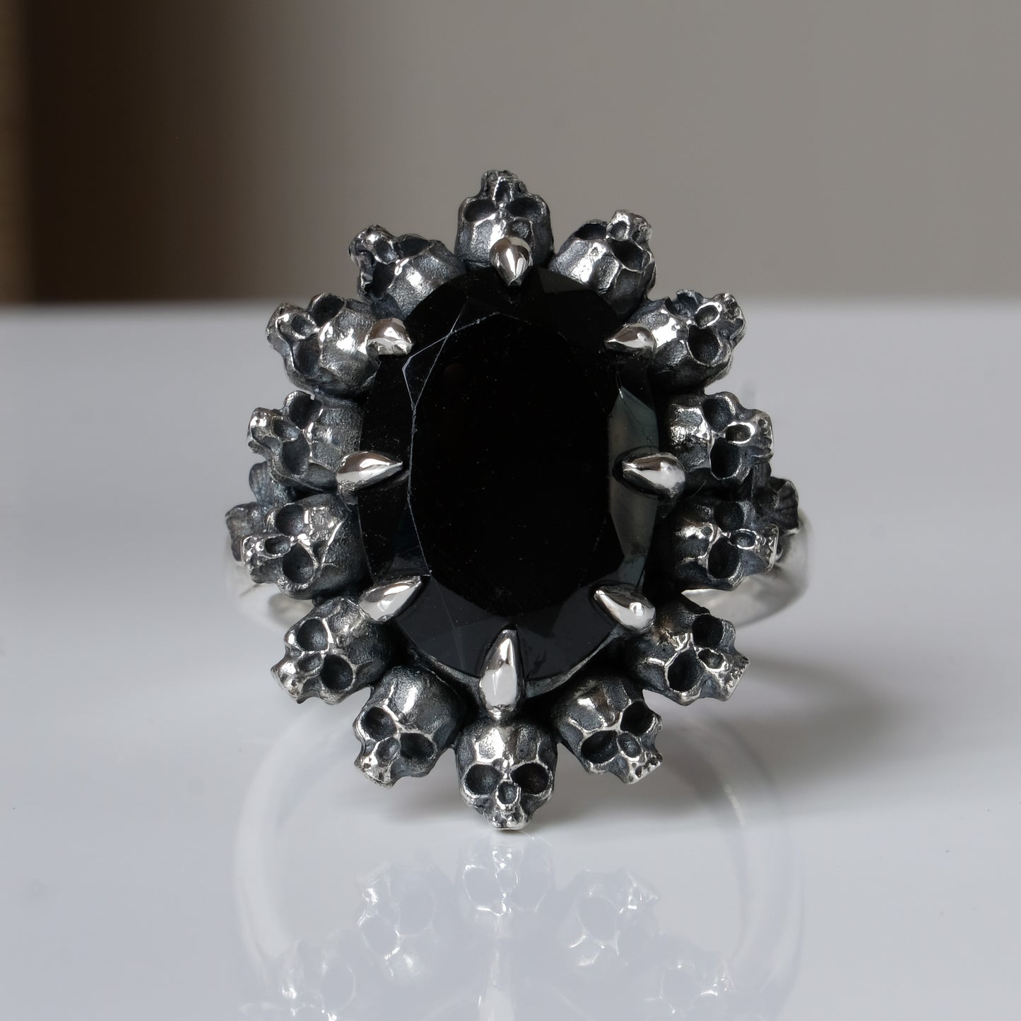 Ring with claw set black spinel gemstone and silver skull design on a white background