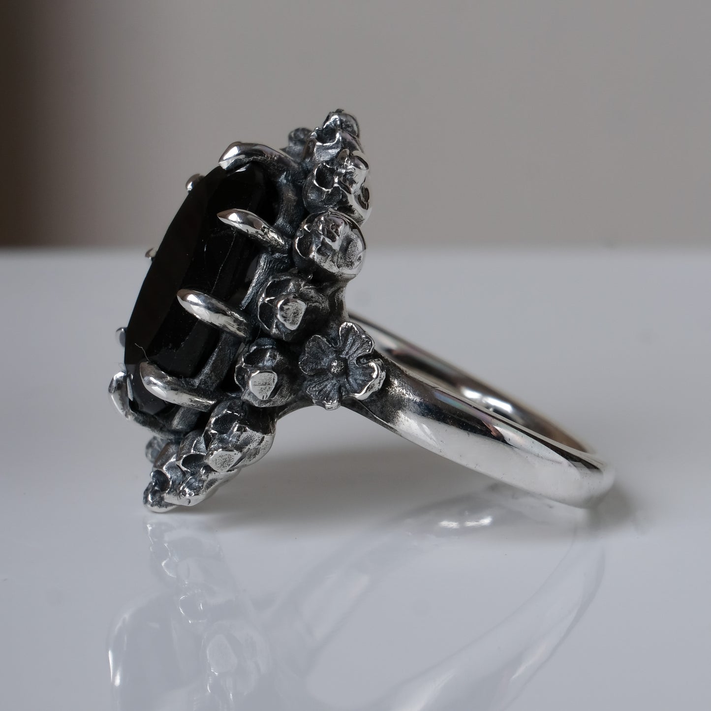 Ring with claw set black spinel gemstone and silver skull design on a white background