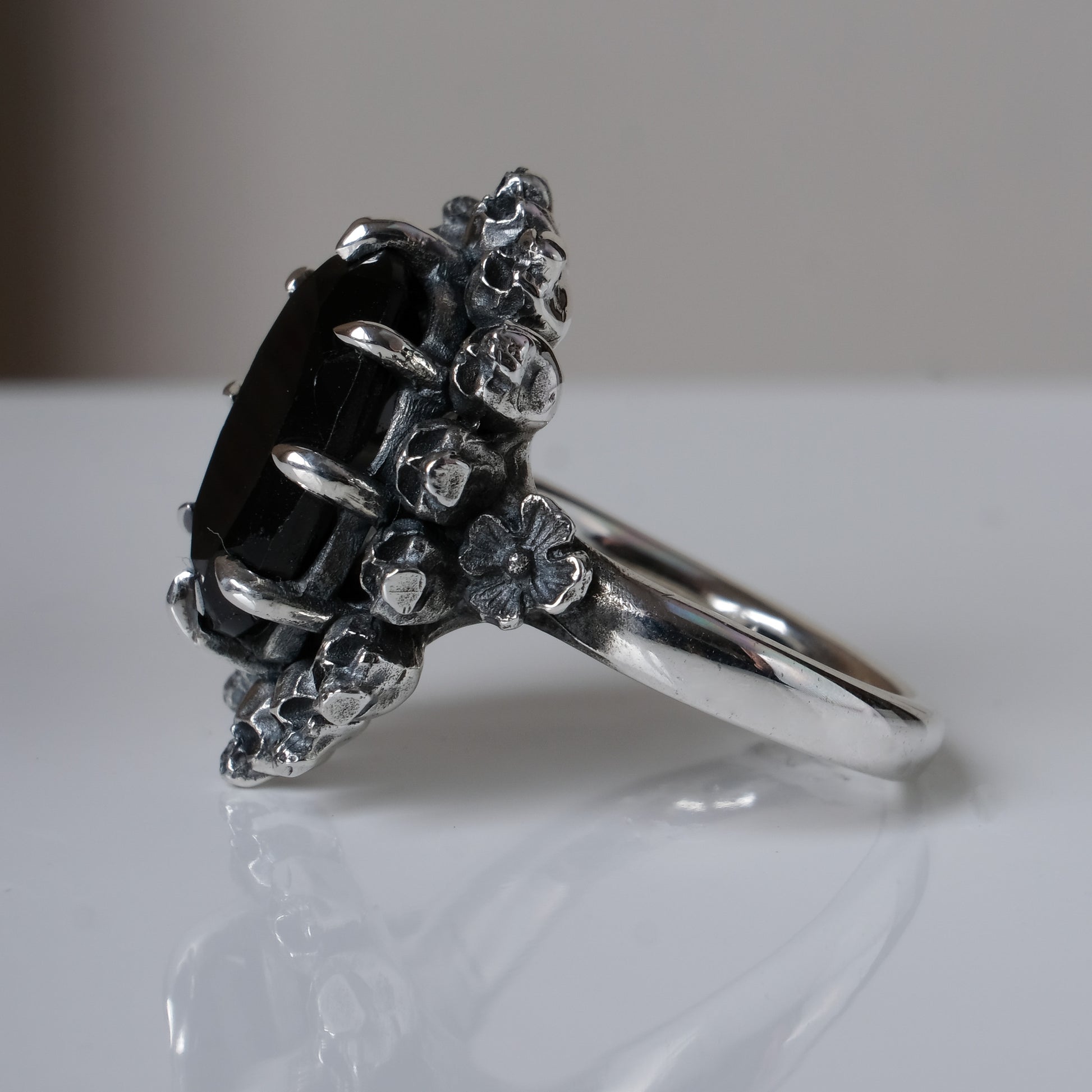 Ring with claw set black spinel gemstone and silver skull design on a white background