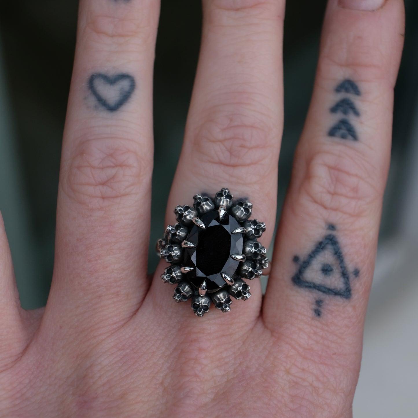 Ring with claw set black spinel gemstone and silver skull design worn on hand with tattoos with neutral background