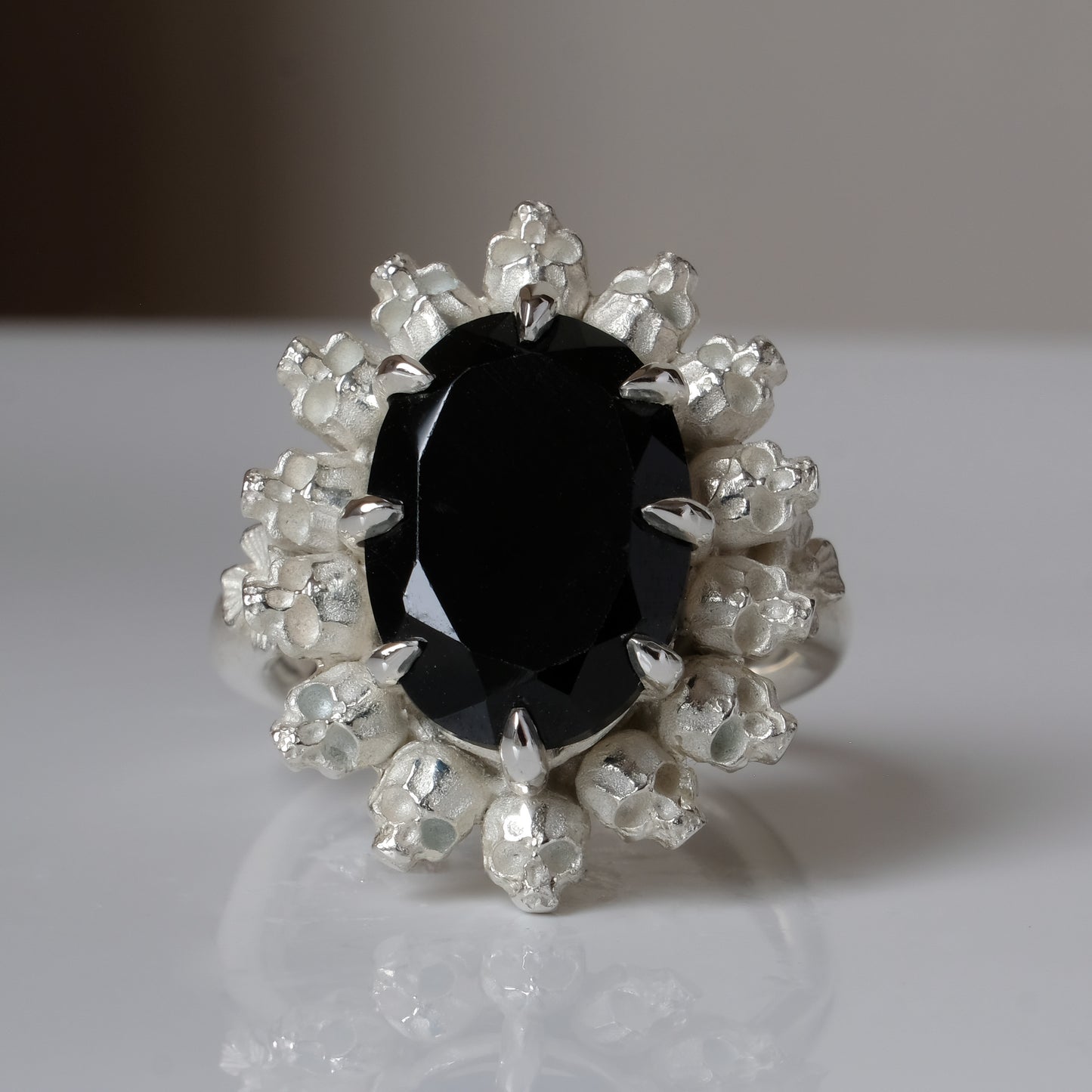 Ring with claw set black spinel gemstone and silver skull design on a white background