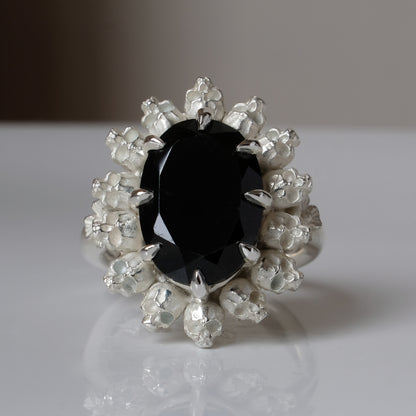 Ring with claw set black spinel gemstone and silver skull design on a white background