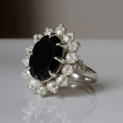 Ring with claw set black spinel gemstone and silver skull design on a white background
