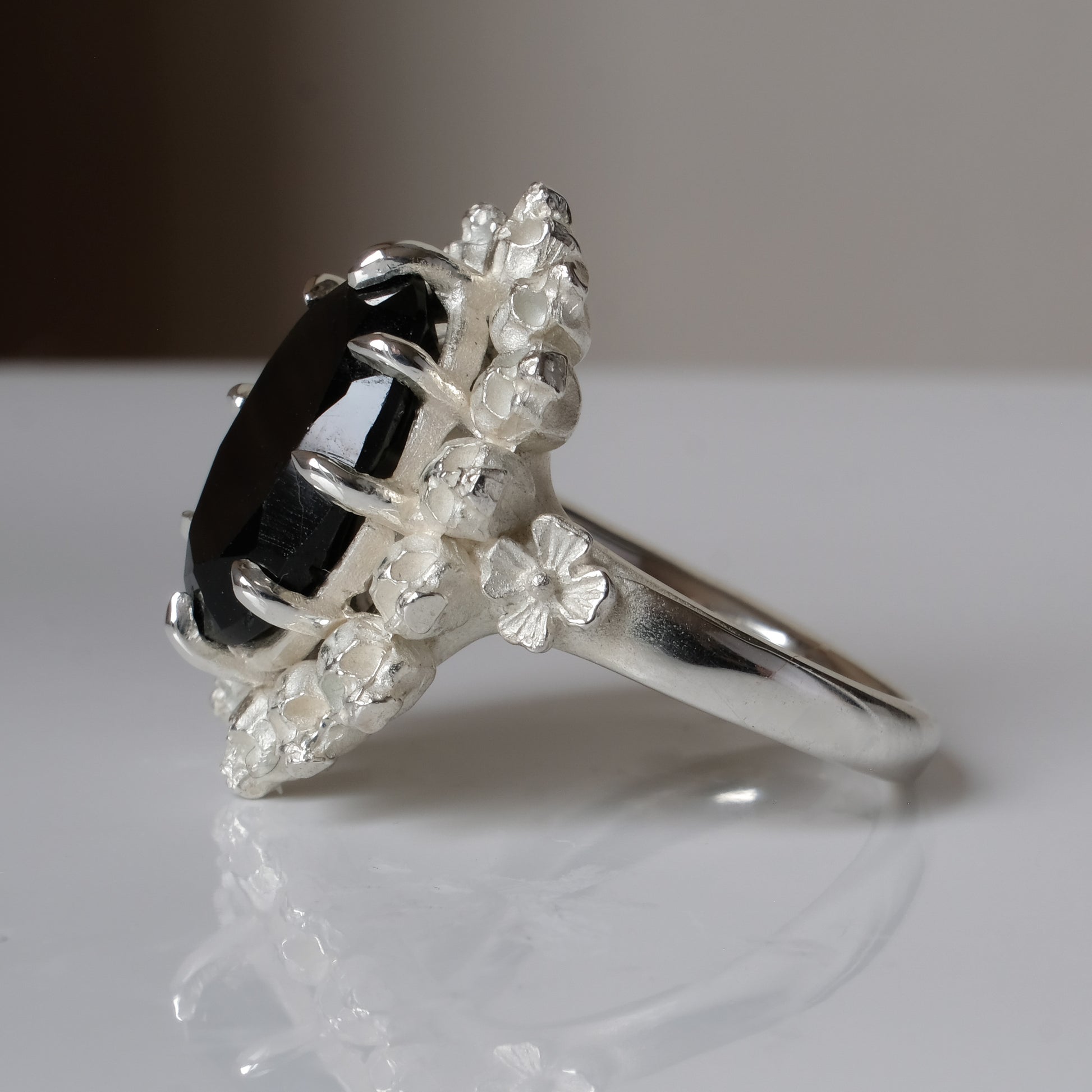 Ring with claw set black spinel gemstone and silver skull design on a white background