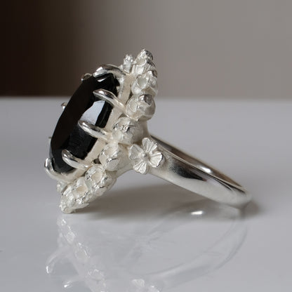Ring with claw set black spinel gemstone and silver skull design on a white background